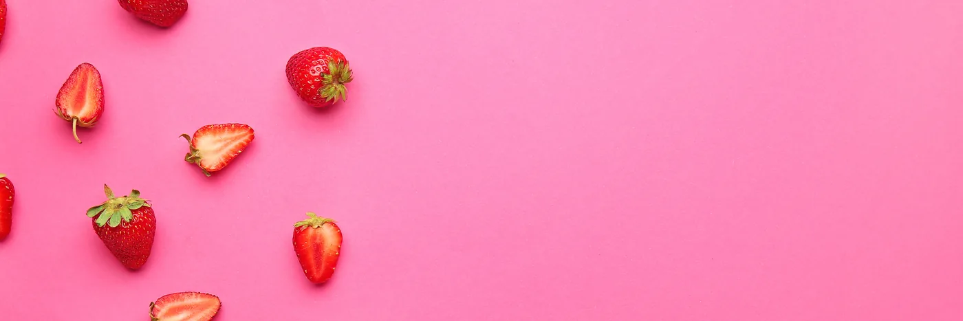 Fresh strawberries scattered across a flat pink background