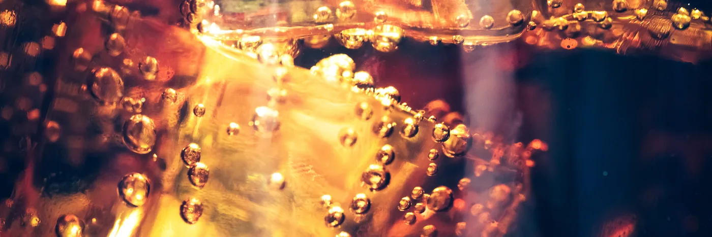 Ice cubes and carbonation bubbles in a glass of amber soda, lit from behind