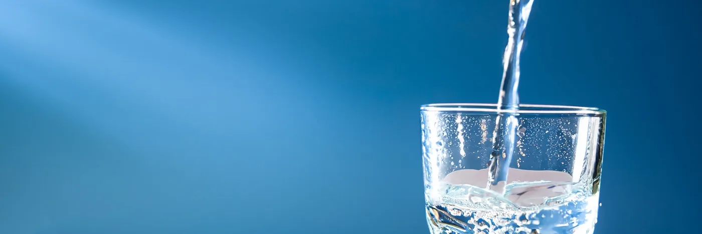 Sparkling water being poured into a clear drinking glass against a blue background