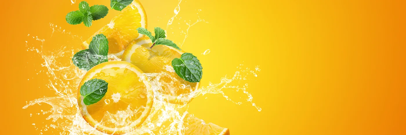 Orange slices and mint suspended in splashing juice against a bright orange background