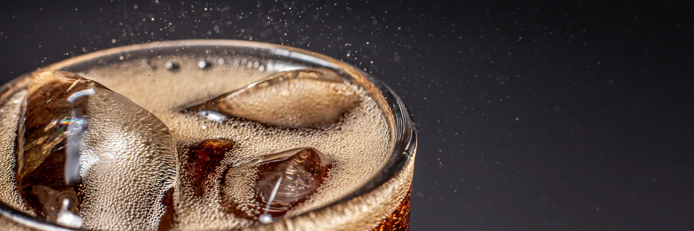 A glass of dark fizzy soda over ice against a black background
