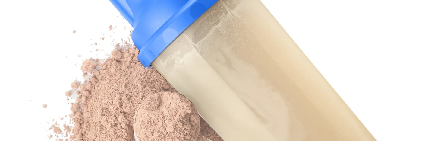 A plastic shaker bottle of mixed protein shake beside a pile of loose protein powder on white
