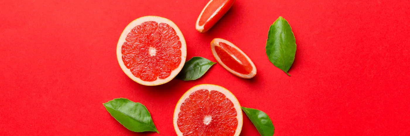 Whole and halved pink grapefruit with leaves on a flat red background