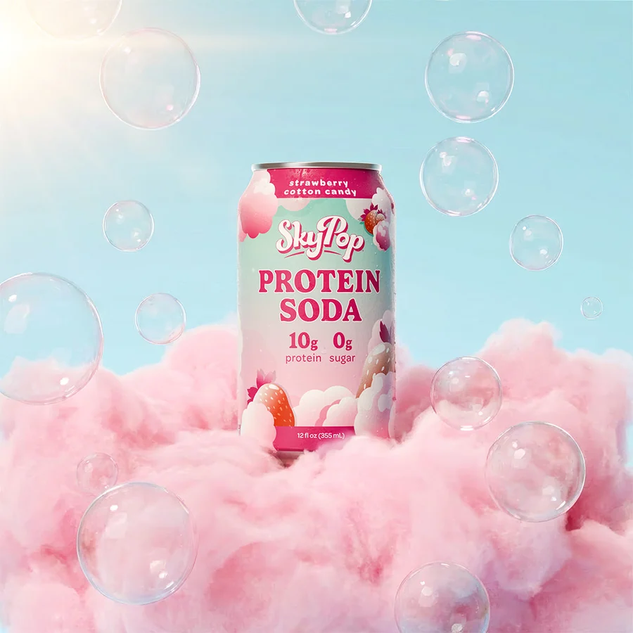 SkyPop Strawberry Cotton Candy protein soda can resting on pink cotton candy under a blue sky