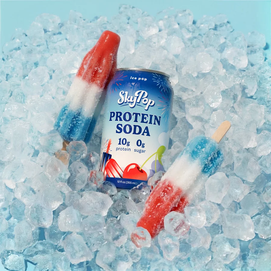 SkyPop Ice Pop protein soda can lying on crushed ice beside red white and blue ice pops